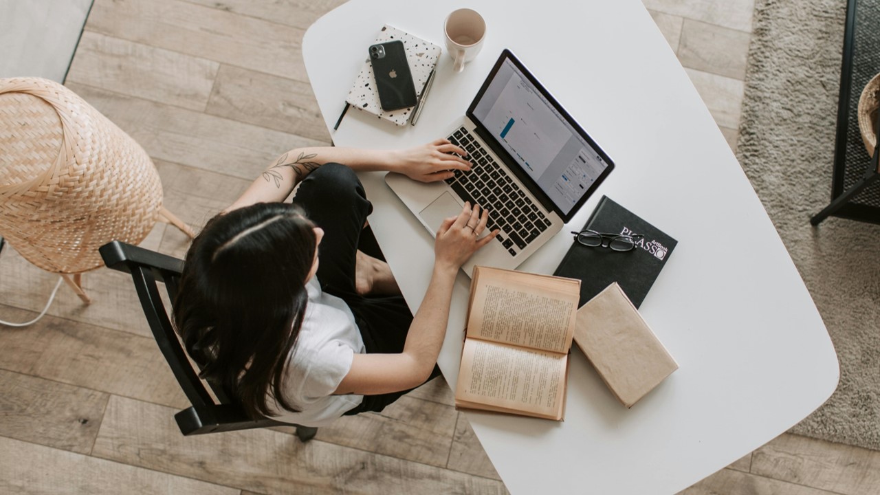 Mulher sentada em mesa com notebook e livros