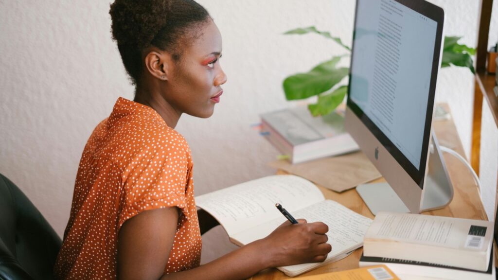 Mulher olhando tela de computador e anotando