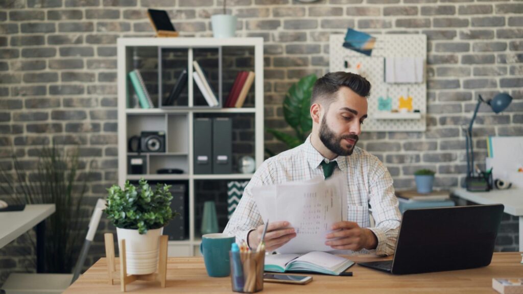 Homem olhando notebook e organizando papéis