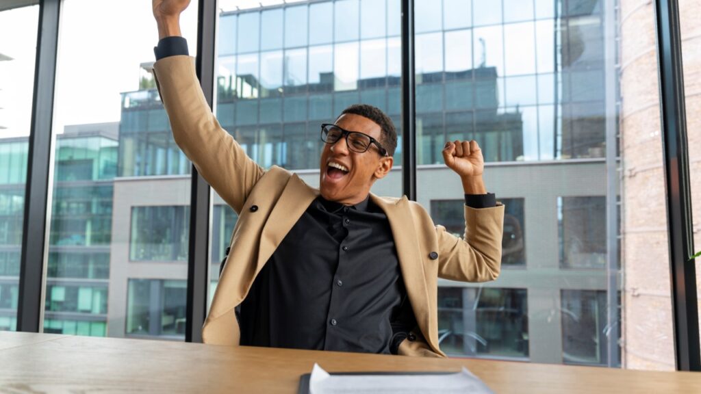 Homem sentado em mesa de empresa comemorando